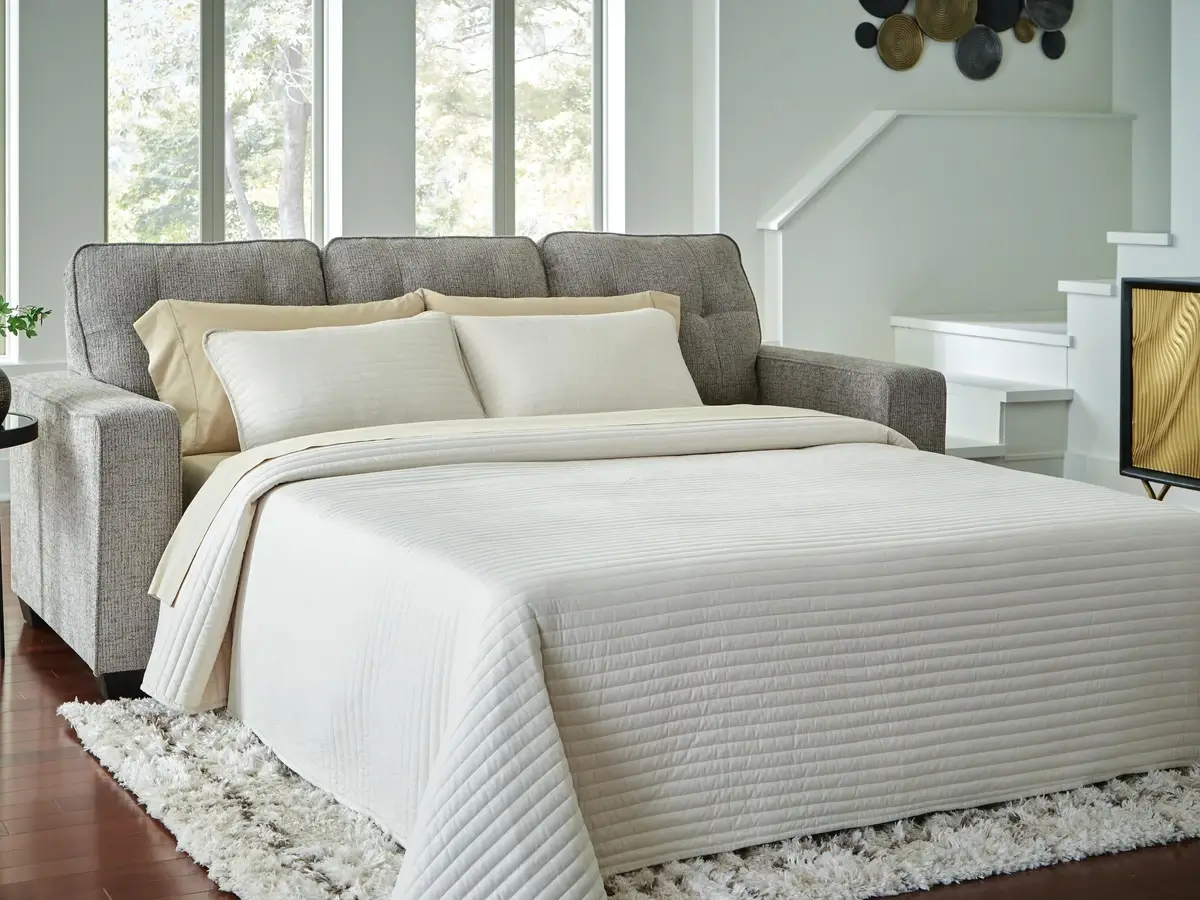 Gray pull-out sofa bed with white textured quilt and pillows.
